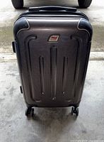 Front view of black Andare small suitcase with hard shell and four spinner wheels on concrete floor.