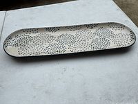 Oval stoneware serving tray with a daisy-like floral pattern in black on a white background, photographed on a table surface.