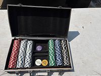 Poker chip set arranged in metal case showing stacks of red, white with blue spots, green, black with white spots, and blue with white spots chips. Three dealer/blind buttons visible in center.