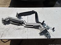 Two adjustable monitor holder arms with metal clamps attached to desk, one black and one silver.