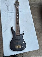 Full view of black Johnson electric bass guitar laid flat on a white table. Shows complete guitar body and neck, four strings, and tuning pegs.