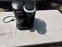 Front view of black Keurig coffee maker showing both glass carafe and pod brewer with power cable visible.