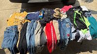 Photo of assorted kids clothing including jeans, t-shirts, jackets and pants laid on ground.