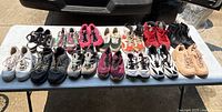 Full view of 14 pairs of assorted shoes arranged on a table outdoors, variety of colors and styles visible