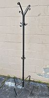 Full view of the metal coat rack showing its height, hooks at the top and middle, and four-legged base.