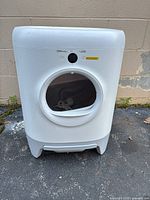 White automatic cat litter box with round door and control button on front, placed outdoors.
