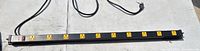 Photo of a black power strip showing 8 yellow electrical outlets along its length, with a power switch and circuit breaker on one end and a power cord with plug.