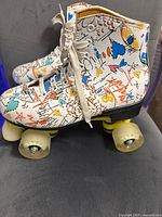 Side view of one white roller skate with graffiti and yellow wheels showing design and lace detail.