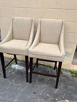 Two beige/tan upholstered counter height barstools with dark wooden legs, shown from front and side angles to highlight condition and design.