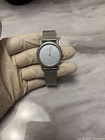 Front view of Skagen Denmark steel analog wristwatch on gloved hand showing the watch face and mesh strap.