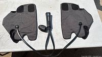 Full view of two gray fabric leg massager sleeves connected by cables to the remote control and power adapter on a white surface.