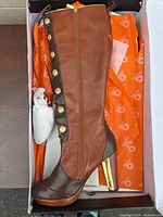 Tall brown leather boots with zipper and decorative lace-up side featuring gold buttons, showing high block metallic gold heels and platform.