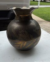 Front and side view of a vintage brass vase with visible floral etched patterns and a rounded body with a wavy rim.