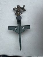 Photo of a vintage Nelson water sprinkler with a metal sprinkler head mounted on a green plastic stake with two holes for ground insertion.