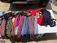 Overhead photo of women's clothing laid out on table showing a variety of folded clothes including shirts, pants, and dresses in multiple colors and patterns.