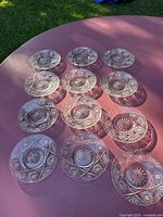 Top-down view showing all 11 crystal saucer plates arranged in rows on a pink surface, highlighting the pattern and clarity of the glass.