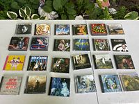 Lot of 24 music CDs including Michael Jackson, Bruce Cockburn, Blondie, others displayed on a white table outdoors with greenery background.