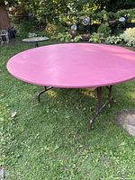 Full view of the round pink folding table set up outdoors on grass with brown folding legs visible.