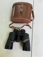 Black 7x35 binoculars with brown leather carrying case on white background.