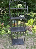 Front view of black wrought iron shelving unit standing outdoors in a garden area.