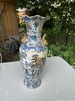 Front and side view of ceramic vase showing blue floral and figurative design and gold handles.