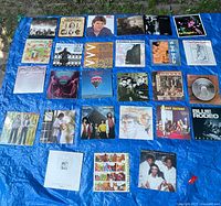 Photo showing 27 vinyl record covers laid out on a blue tarp. Various artists and genres represented with mixed sleeve conditions.