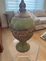 Front view of the lidded terracotta urn showing the green glazed upper half, classical textured midsection with acanthus leaf trim, pedestal base, and sculpted finial top on lid.