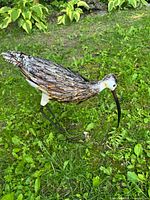 Side view of the metal bird sculpture showing detailed layered feathers and long curved beak with painted rustic finish.