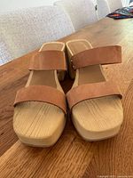 Pair of caramel leather strap platform sandals showing front and top view on wooden surface.