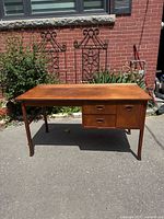 Front view of teak desk showing overall design, three recessed oval drawer pulls