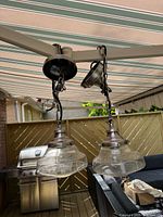 Pair of brushed nickel hanging pendant lights with large clear glass bell-shaped shades hanging from a frame in outdoor setting.