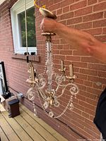 Held vintage chandelier showing front and side view, brass arms with scroll design and ribbed glass column with crystal bead chains and prisms.