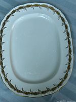 Top view of elongated oval bone china platter showing gold laurel garland border with scalloped gold-trimmed edge on white background.