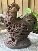 Front angle showing detailed openwork cast iron rooster with rust patina and ring handle.