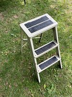 Side view of vintage white metal 2-step folding ladder showing anti-slip pads on steps and sturdy frame.