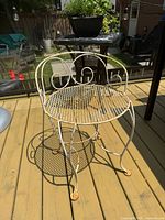 Vintage wrought iron patio chair with white paint, round mesh seat, scrollwork on back and arms, and surface rust on feet and legs, shown on an outdoor deck.
