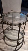 Full view of the antique brass circular glass stand showing top and bottom glass shelves with brass rims and wheels.