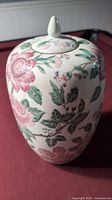 Full view of ceramic jar with floral design and lid on, showing pink flowers and green leaves on cream ceramic.