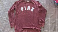 Pink faded sweatshirt with PINK lettering front view laid flat on a bedsheet