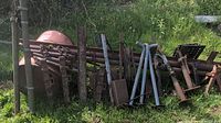 Wide view of the lot showing various steel rods, metal barrel, chains, and structural steel parts in grassy outdoor area.