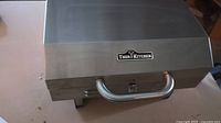 Closed view of the portable BBQ showing stainless steel exterior, handle, and Thor Kitchen logo.