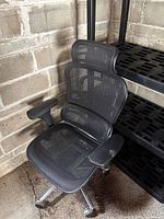 Front view of black mesh ergonomic office chair beside shelving