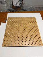 Full view of square tan slotted pegboard panel on white background