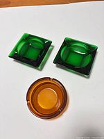 Overview of two green square and one amber round glass ashtrays