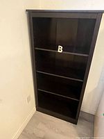 Front view of tall dark brown bookcase with four shelves