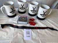 Four white ceramic mugs with hockey puck motif, four coasters, three red whistles and a black commemorative lanyard