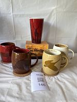 All four ceramic mugs and travel mug arranged with cork coasters and Tim Hortons box.