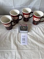 Four brown Tim Hortons ceramic mugs with cream interior arranged behind four Ottawa Senators hockey puck coasters in original clear plastic box on a white surface, with lot label visible.