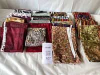 Top view of multiple folded 100% cotton fabric pieces arranged in rows with visible distinct patterns and packaging tags.