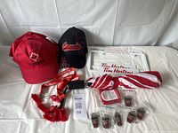 Photo showing 3 red Canada baseball hats, 1 black Canada baseball hat, 6 metal Tim Hortons keychains, 6 red whistles on lanyard, and 2 Tim Hortons license plate holders arranged on white surface.